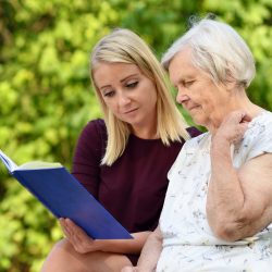 Young woman reading a book elderly woman in the park. MANY OTHER PHOTOS WITH THIS SENIOR MODEL IN MY PORTFOLIO.